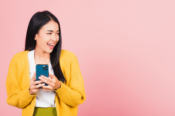 Wall Mural - Happy Asian portrait beautiful cute young woman teen smiling excited using smart mobile phone studio shot isolated on pink background, Thai female surprised making winner gesture on smartphone