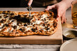 © The Picture Pantry - Hand slicing a mushroom, onion and sausage pizza on a cutting board.