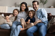 © fizkes - Married young couple and preschool siblings sitting on sofa relaxing together at modern home smiling looking into distance. Adoption and custody, young homeowners family portrait, bank loan concept