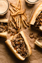 Cheesesteaks And Fries On Parchment Paper With Glasses Of Dark Beer.