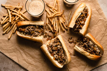 Cheesesteaks And Fries On Parchment Paper With Glasses Of Dark Beer.