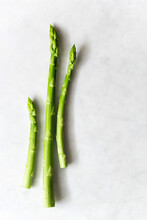 Three Asparagus Spears On A White Marble Background.