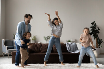 Untroubled family with little children dancing together in living room, full-length view, people enjoy weekend, comfort home, having fun relish festive mood celebrate relocation to first house concept