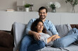 © fizkes - Beautiful millennial couple relax on comfy sofa in living room hugging pose look at camera, enjoy weekend at new first home. Homeowners portrait, bank loan for young family, romantic relations concept