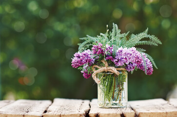 Wall Mural - Lilac flowers in glass jar on wooden table. Copy space