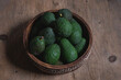 freshly harvested green avocados lie in a wooden bowl on a rustic wooden table