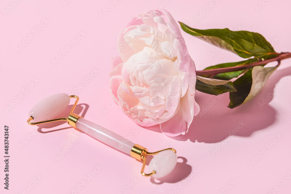 Face massage roller with peony flower on color background
