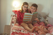 Teen brother and sister reading book in bed