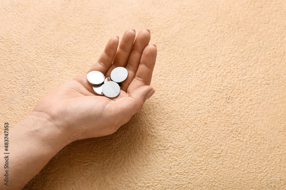 Woman holding lithium button cell batteries on beige background