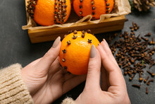 Woman Making Handmade Christmas Decoration Made Of Tangerine With Cloves On Dark Background, Closeup