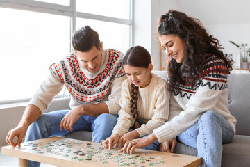 Wall Mural - Happy parents with little daughter in warm sweaters doing puzzle at home