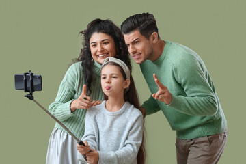 Sticker - Happy parents with little daughter in warm sweaters taking selfie on green background