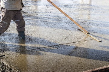 Construction worker leveling a poured concrete floor in an industrial workshop. Legs in boots in concrete. Surface concreting. Monolithic reinforced concrete works.