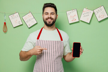 Poster - Young chef confectioner baker man in striped apron using point on mobile cell phone look for recipe blank screen workspace area isolated on plain pastel light green background. Cooking food concept.