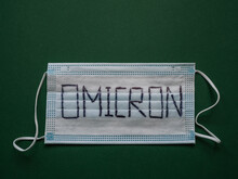 Face Mask With Word Omicron Written On It And Green Background With Copy Space