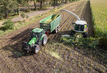 Wall Mural - Luftfoto - Maishäcksler und Transportfahrzeuge auf dem Feld bei der Maisernte.
