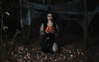Sexy halloween portrait of brunette haired woman with hat on her head, makeup with fake blood. Dark forest background.