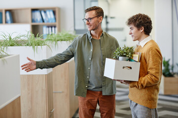 Portrait of smiling male manager welcoming new employee in office and showing workplace, copy space