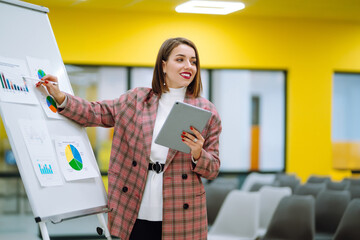 Wall Mural - Young woman leader, presenter, make a business presentation at a conference in the office, business woman mentor explaining a graphic diagram on a flipchart, corporate group seminar.