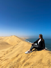 A young woman sitting at sandy dunes on seashore. Sandwich Harbour in Namibia.