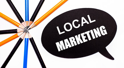 On a light background, multi-colored pencils and on a black background a white card with the text LOCAL MARKETING