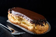 Single eclair with chocolate and a fork on a dark slate