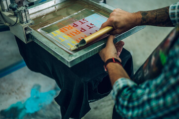 Male worker pressing ink on frame while using the printing machine in a workshop