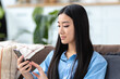 © kucherav - Young Asian woman using a mobile phone on the couch at home