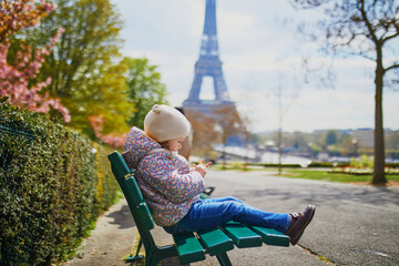 Wall Mural - Adorable three year old girl sitting on the bench near the Eiffel tower in Paris, France