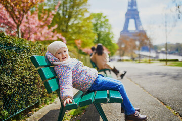 Wall Mural - Adorable three year old girl sitting on the bench near the Eiffel tower in Paris, France