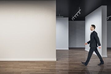 Aufkleber - Businessman walking in modern concrete exhibition hall interior with mock up place on wall and wooden flooring with reflections. Art and museum concept.