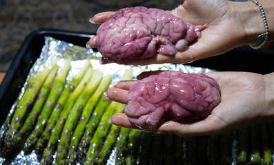 Fototapeta raw bloody brains in the hands of a girl. a girl holds brains in her hands in the kitchen against the background of green asparagus. high quality photo