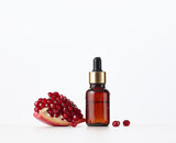 Fototapeta Tulipany - brown glass bottle with a pipette and red pomegranate seeds on a white background. Template for cosmetic liquid products, advertising and promotion