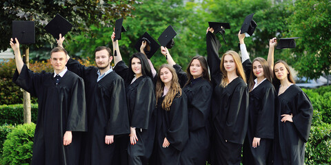 group of university or college graduates in black robes raised their hands with square caps of graduates and are happy about the graduation.