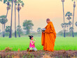 Buddhist monk going about with alms bowl to receive food and girl giving food to monk in morning in Thailand