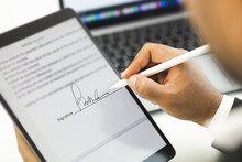 Close Up Businessman Hand Electronic Signature On Tablet By Stylus. Write Business Agreement Of Contract. Man Signing Contract On Tablet. Business And Technology Concept.