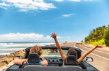 Fototapeta Londyn - Road trip car holiday happy couple driving convertible car on summer travel Hawaii vacation. Woman with arms up having fun, young man driver