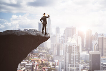 Canvas Print - Attractive young european male on cliff edge looking into the distance on bright city background with daylight and mock up place. Future, success, leadership and career growth concept.