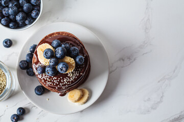 Poster - Chocolate pancakes with chocolate cream and blueberries, white kitchen table background.