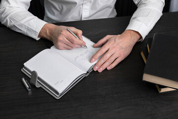 Poster - Man hands holding pen and writing in planner. Businessman sitting at desk with books or codes. Business and education concept . High quality photo