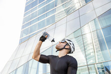 Thirsty cyclist drinking water from bottle in front of office building