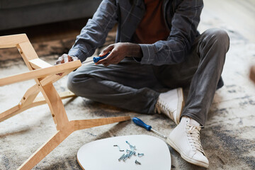 Cropped shot of young African-American man assembling furniture at home, copy space