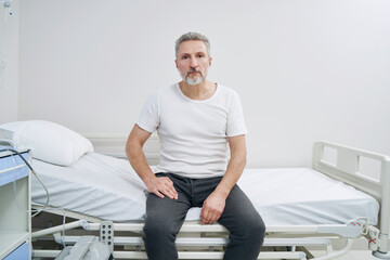 Wall Mural - Sad female patient seated alone on hospital bed staring ahead