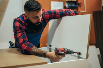 Wall Mural - Young male carpenter working in workshop while using power drill