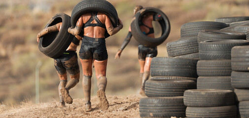 Wall Mural - Mud race runners. Runners carrying tires in a test of the race