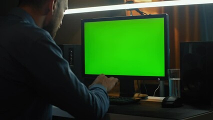 A man works in front of a computer with a green screen.
