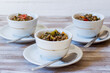 Lentil and escarole soup served in white cups on white wooden background