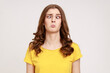 Portrait of attractive funny silly young woman in yellow T- shirt with cross eyed, has stupid dumb face, awkward confused comical expression. Indoor studio shot isolated on gray background.