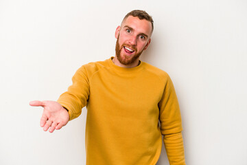 Young caucasian man isolated on white background stretching hand at camera in greeting gesture.