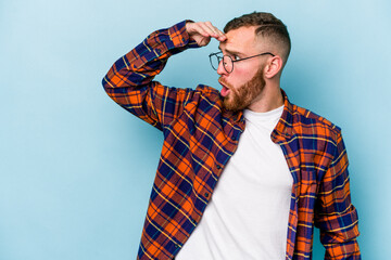 Young caucasian man isolated on blue background looking far away keeping hand on forehead.